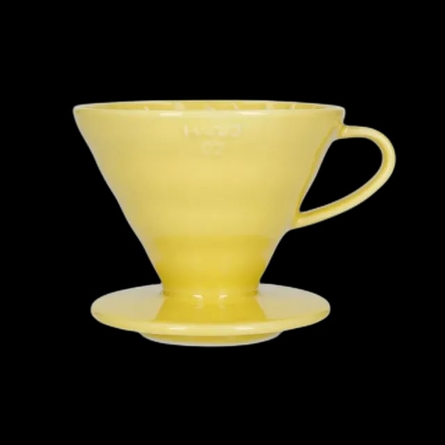 Klasyczny ceramiczny dripper Hario V60-02 w żywym żółtym kolorze, zaprojektowany do precyzyjnego parzenia kawy metodą pour-over. Stożkowy kształt i spiralne żłobienia wewnętrzne zapewniają optymalną ekstrakcję, podkreślając bogaty smak i aromat kawy.
