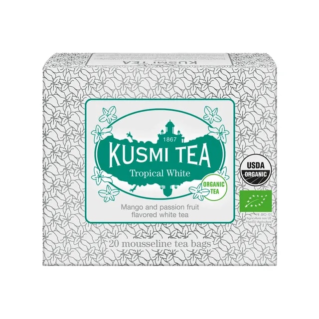 Kartonowe opakowanie herbaty Kusmi Tea Tropical White zawierające 20 saszetek, z ozdobną białą grafiką kwiatową i zielonym logo, oferujące organiczną białą herbatę o smaku mango i marakui.
