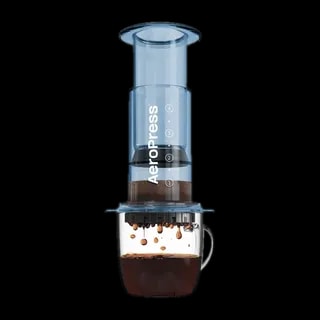 Zdjęcie niebieskiego zaparzacza AeroPress Clear Blue, umieszczonego na szklance z zaparzaną kawą. Krople kawy spadają do kubka, ukazując proces parzenia metodą AeroPress, z przezroczystym niebieskim korpusem urządzenia.