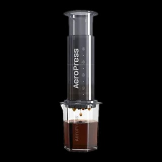 Zdjęcie czarnego zaparzacza AeroPress XL, umieszczonego na szklance, pokazującego proces parzenia kawy. Krople kawy delikatnie spadają do kubka, podkreślając wyjątkową metodę parzenia metodą AeroPress, z większym korpusem dla większej ilości kawy.