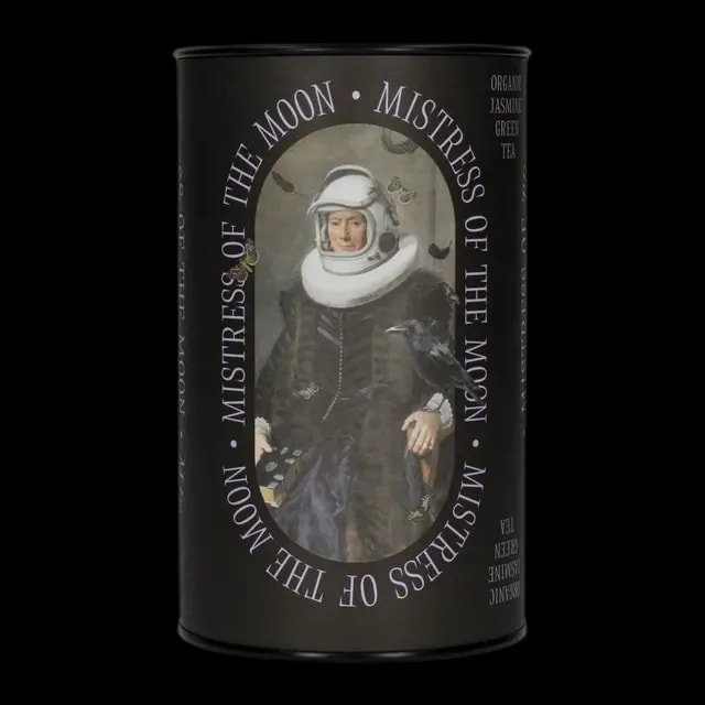 Puszka herbaty zielonej Leaf Liturgy „Mistress of the Moon” o smaku jaśminowym. Czarne opakowanie w kształcie cylindra ozdobione surrealistyczną grafiką kobiety w renesansowym stroju i hełmie astronauty, z krukiem siedzącym na ręce i unoszącymi się wokół motylami. Herbata organiczna, waga 60 g.